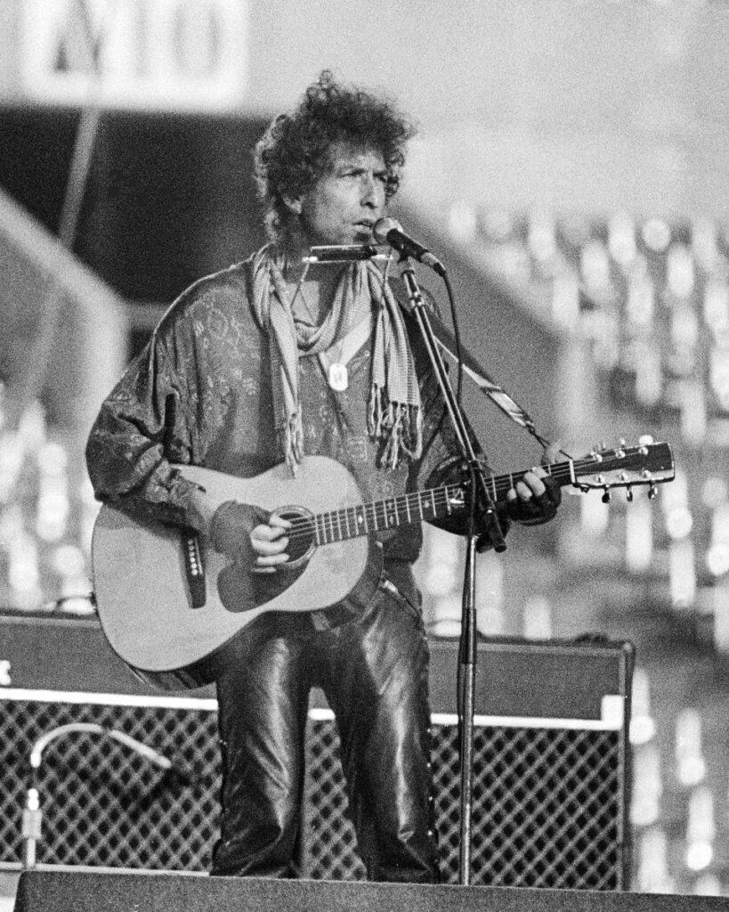 Bob Dylan playing acoustic guitar and harmonica at Rich Stadium, Buffalo NY, July 4, 1986 - concert photography by Chuck Spang